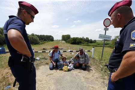 Police guard migrants from Syria who have crossed the border from Serbia to Hungary, walking on the dam near the Tisza river near the city of Szeged, Hungary, on June 29, 2015. REUTERS/Laszlo Balogh