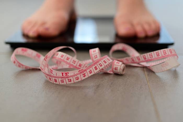 Two feet standing on a weight scale with measuring tape next to it