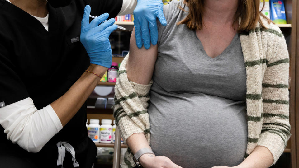 A pregnant woman receives a shot in the upper arm