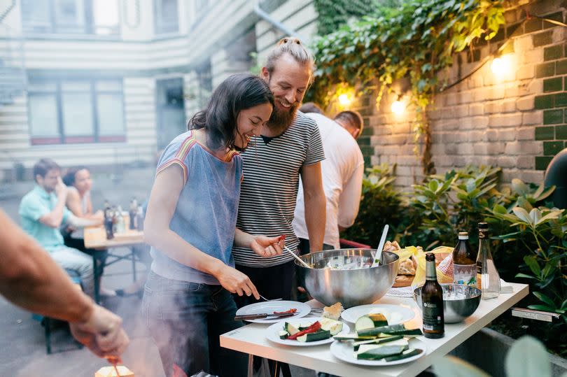 A young couple having a barbecue with their friends are getting plates ready and preparing food.