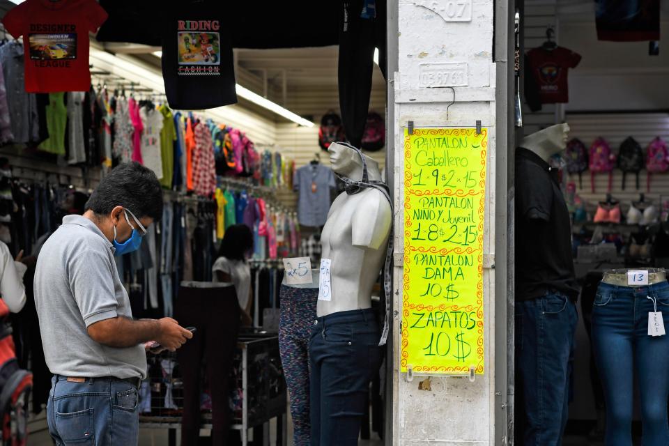 A man uses a mobile phone in front of a sign displaying prices in US dollars outside a clothing store in Caracas on December 9, 2020. - In Venezuelan nobody wants bolivars, the weakened national currency. Everything can be payed for in dollars, which have been prohibited for 15 years, but keep gaining power in a country hit by years of recession and hyperinflation. (Photo by Federico PARRA / AFP) (Photo by FEDERICO PARRA/AFP via Getty Images)