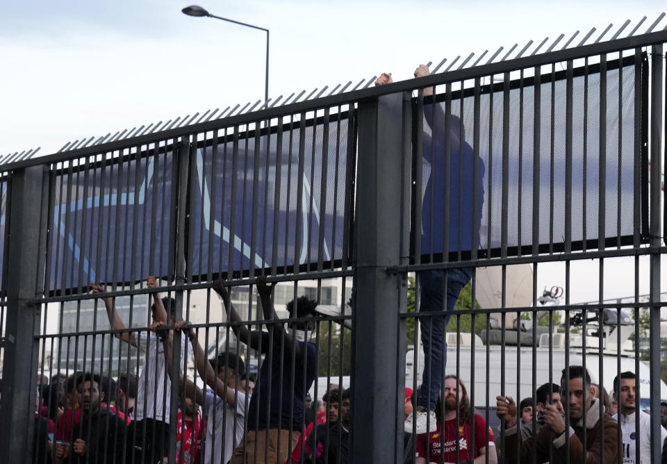 A fan climbs on the fence in front of the Stade de France prior the Champions League final soccer match between Liverpool and Real Madrid, in Saint Denis near Paris, Saturday, May 28, 2022. Police have deployed tear gas on supporters waiting in long lines to get into the Stade de France for the Champions League final between Liverpool and Real Madrid that was delayed by 37 minutes while security struggled to cope with the vast crowd and fans climbing over fences. (AP Photo/Christophe Ena)