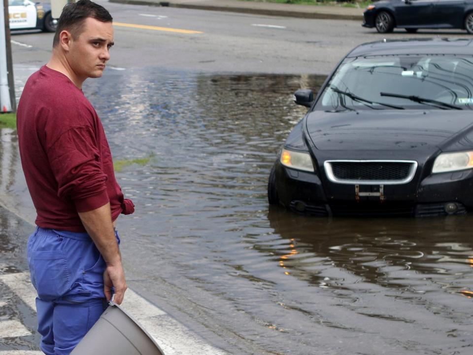 A man holds a bucket in front of his car, which stalled in floodwaters in Lodi, New Jersey (Kevin R Wexler/AP)
