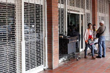 A woman walks out of a supermarket with its security shutters partially closed as a precaution against riots or lootings, in San Cristobal, Venezuela January 16, 2018. REUTERS/Carlos Eduardo Ramirez