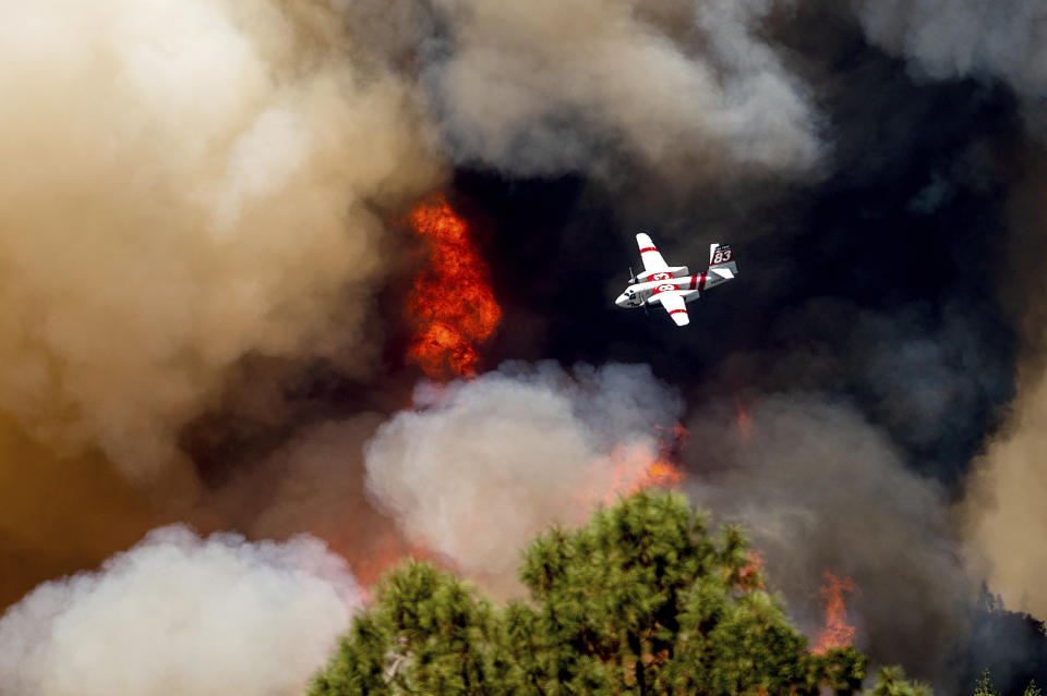An air tanker flies over clouds of smoke and flames.