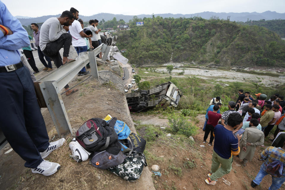 People watch as a rescue team inspects the wreckage after a bus carrying Hindu pilgrims to a shrine skid off a highway bridge into a Himalayan gorge near Jammu, India, Tuesday, May 30, 2023. (AP Photo/Channi Anand)