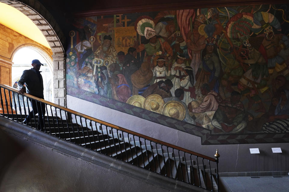 Historian Jonatan Chavez descends a flight of stairs past a mural by Fernando Leal titled, “Los danzantes de Chalma”, at the former Jesuit college Antiguo Colegio de San Ildefonso in Mexico City, Wednesday, April 26, 2023. Leal portrays what syncretism brought after the Spanish conquest: religious festivities where sacred and profane symbols blend. According to Chavez, murals like these will never lose relevance because they are a way to understand how history triggers a constant redefinition of spaces. (AP Photo/Marco Ugarte)