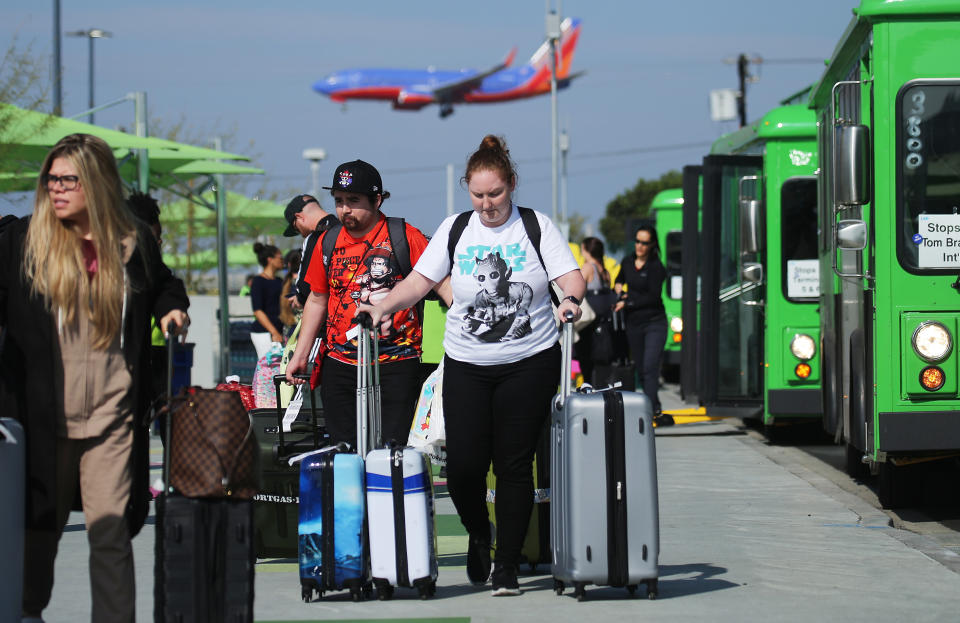 LOS ANGELES, CALIFORNIA - NOVEMBER 06: Arriving passengers walk with their luggage as they prepare to board vehicles at the new 'LAX-it' ride-hail passenger pickup lot at Los Angeles International Airport (LAX) on November 6, 2019 in Los Angeles, California. The airport has instituted a ban on Lyft, Uber and taxi curbside pickups as airport construction increases during a modernization program. Passengers have complained of long wait times and confusion at the pickup area, especially during peak hours. Passengers must depart their terminal and then ride a shuttle bus or walk to the separate pickup lot. (Photo by Mario Tama/Getty Images)