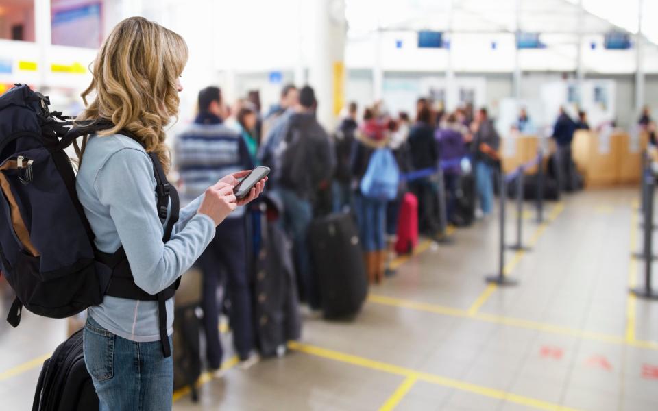 Traveller texting at airport check-in desk - Andrew Bret Wallis/Getty