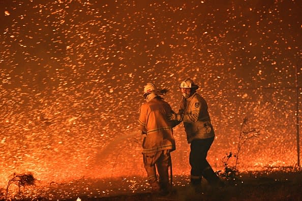 This picture taken on December 31, 2019 shows firefighters struggling against the strong wind in an effort to secure nearby houses from bushfires near the town of Nowra, NSW.