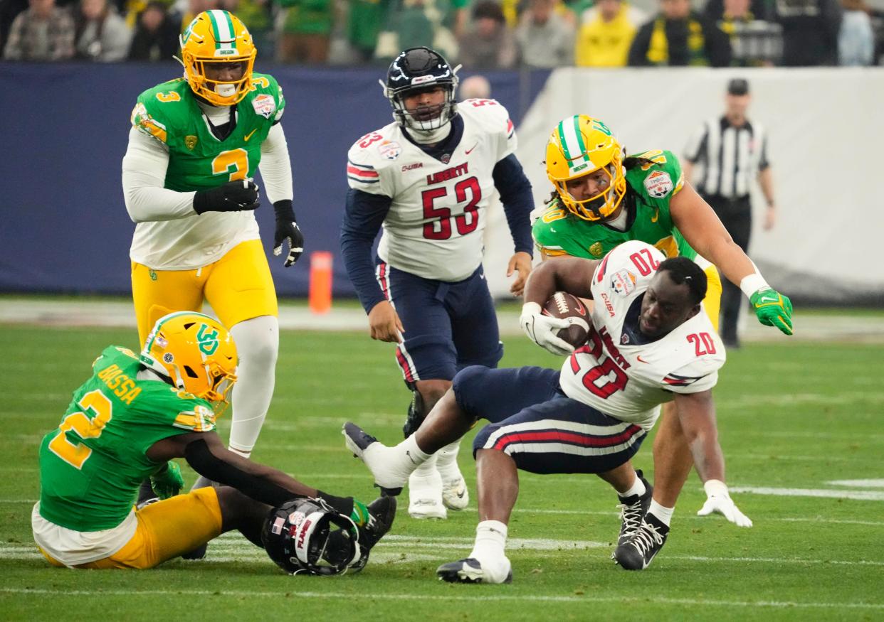 Liberty Flames running back Quinton Cooley (20) loses his helmet after being tackled by Oregon Ducks linebacker Jeffrey Bassa (2) in the first half during the Fiesta Bowl at State Farm Stadium in Glendale on Jan. 1, 2024.