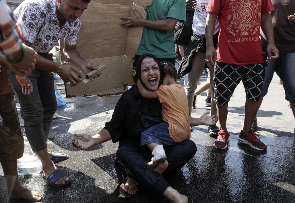 A woman reacts as a girl hugs her during minor clashes between riot police and migrants near Mytilene town, on the northeastern island of Lesbos, Greece, Saturday, Sept. 12, 2020. Thousands of asylum-seekers spent a fourth night sleeping in the open on the Greek island of Lesbos, after successive fires destroyed the notoriously overcrowded Moria camp during a coronavirus lockdown. (John Liakos/InTime News)