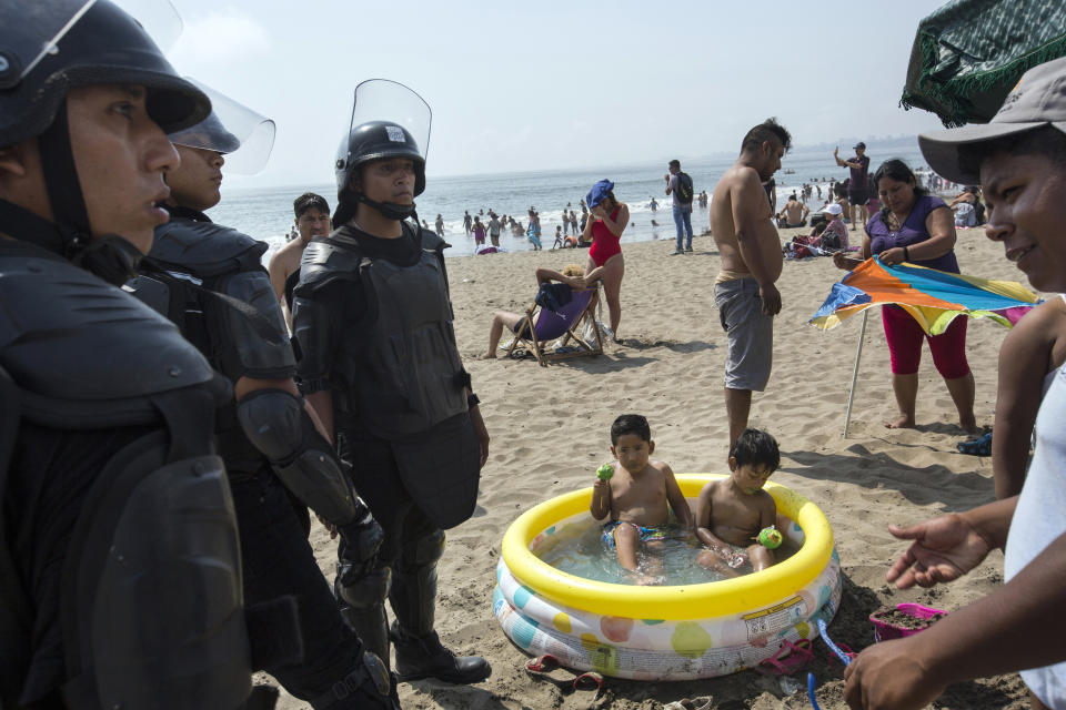 In this Feb. 15, 2020 photo, boys sit in an inflatable pool while eating green sugar-coated apples as policemen work to remove an unlicensed food vendor, at Agua Dulce beach in Lima, Peru. (AP Photo/Rodrigo Abd)