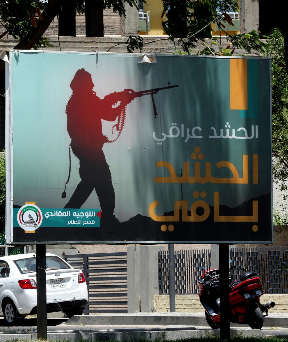 In this Tuesday, July 2, 2019 photo, motorists pass by a Popular Mobilization poster in Baghdad, Iraq. The Iraqi government's move to place Iranian-backed militias under the command of the armed forces is a political gamble by a prime minister increasingly caught in the middle of a dangerous rivalry between Iran and the U.S., the two main power brokers in Iraq. (AP Photo/Hadi Mizban)