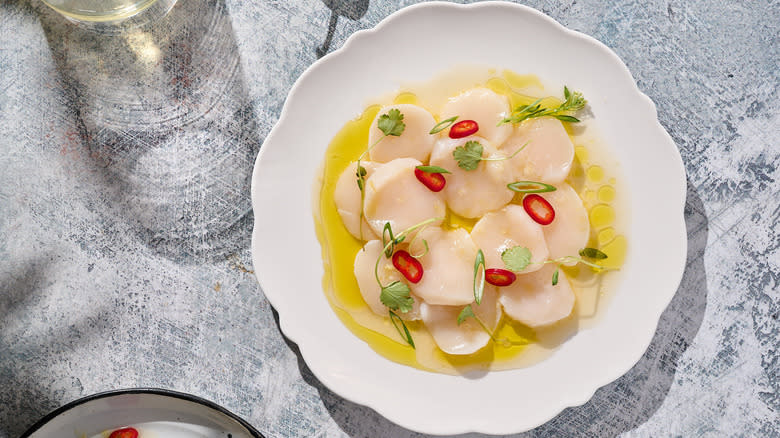 scallop crudo with yuzu, cilantro and chile on white plate