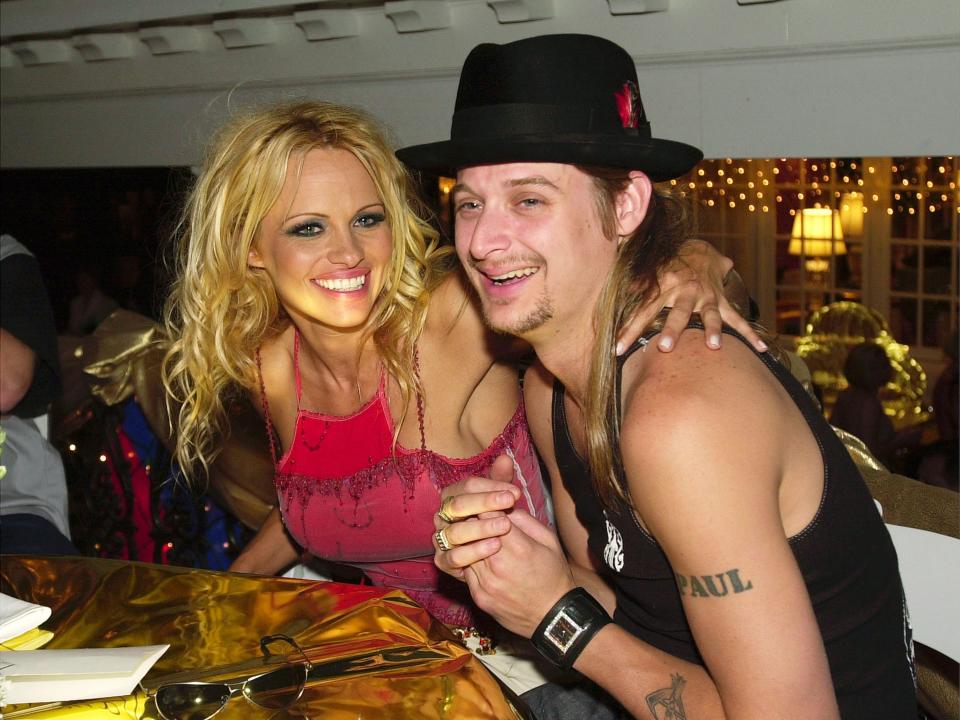 Pamela smiling in a pink halter top and Kid Rock wearing a fedora and tank top.