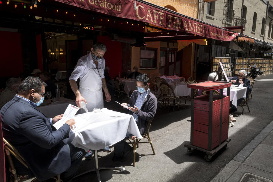 Image: Guests wear protective masks as a waiter serves drinks at a restaurant in San Francisco on June 15, 2020. (David Paul Morris / Bloomberg via Getty Images file)