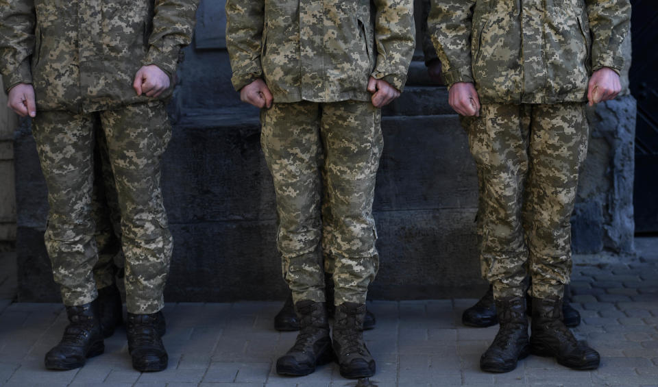 Soldiers in uniform stand in a row at a funeral.