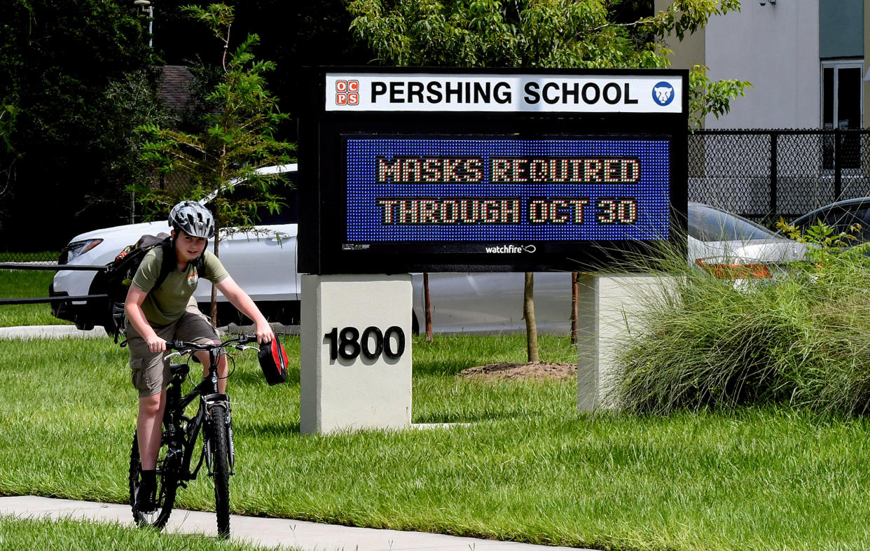 A boy rides his bicycle past a sign at Pershing School in Orlando, Fla., advising that face masks are required for students through Oct. 30, 2021.