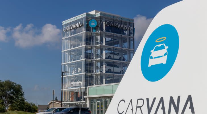 Carvana (CVNA stock) logo on white object in foreground as well as a high-rise building in the background