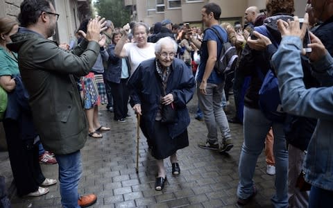 People applaud an elderly woman after voting in a polling station in Barcelona - Credit:  AFP