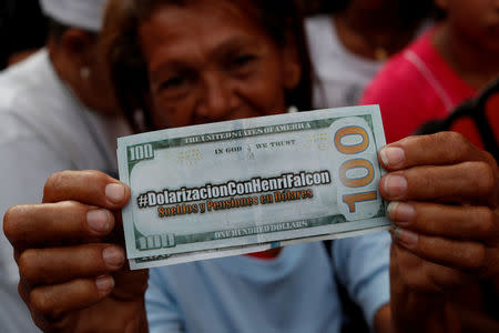 FILE PHOTO: A supporter of Venezuelan presidential candidate Henri Falcon, holding a fake hundred dollar bill that reads, "Dollarization with Henri Falcon" and "Salaries and pensions in dollars", takes part in a campaign rally in Caracas, Venezuela May 14, 2018. REUTERS/Carlos Garcia Rawlins/File Photo