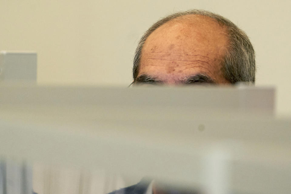 One of the defendants, Anwar R. (57), sits in the dock of the Higher Regional Court behind Corona protective screens, hiding his face under a hood in Koblenz, Germany, Thursday, April 23, 2020. Two former members of Syria's secret police go on trial Thursday in Germany accused of crimes against humanity for their role in a government-run detention center where large numbers of opposition protesters were tortured.(Thomas Frey/dpa via AP)