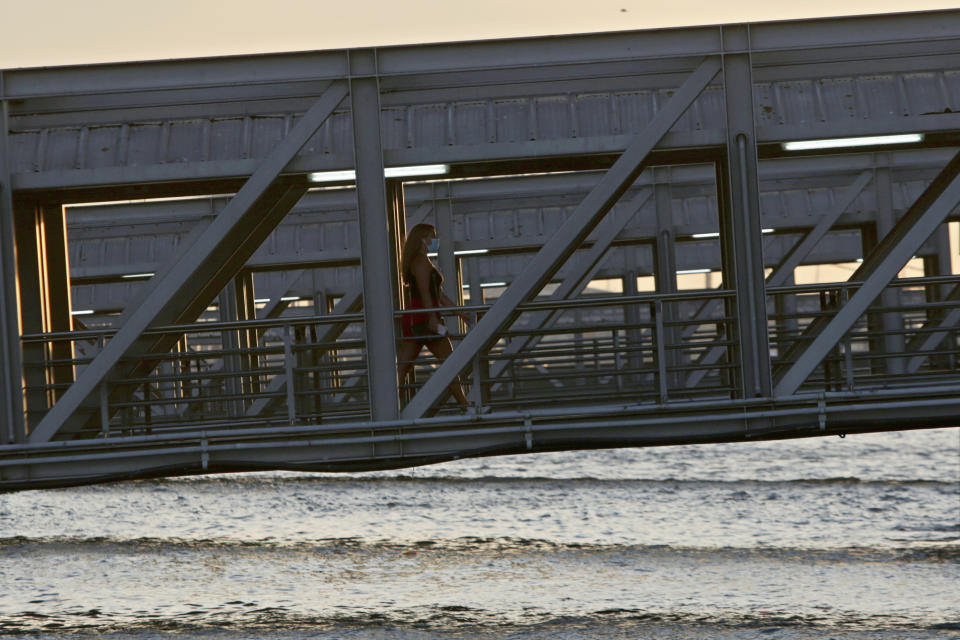 A woman wearing a face mask walks up a gangway disembarking from a ferry arriving in Lisbon from across the Tagus river at sunset, Thursday, Sept. 10, 2020. The Portuguese government is imposing new curbs in the sale and consumption of alcohol and limits on socialization amid a recent increase of coronavirus infections. (AP Photo/Armando Franca)