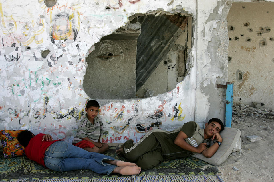 FILE - In this Aug. 10, 2005 file photo, Palestinians rest in the shade of a building destroyed during the Palestinian Intifada, on the outskirts of Khan Younis, near the Israeli settlement of Neve Dekalim. Western countries are reeling from the coronavirus pandemic, awakening to a new reality of economic collapse, overwhelmed hospitals and home confinement. But for millions across the Middle East and in conflict zones elsewhere, much of this is familiar. (AP Photo/Karel Prinsloo, File)