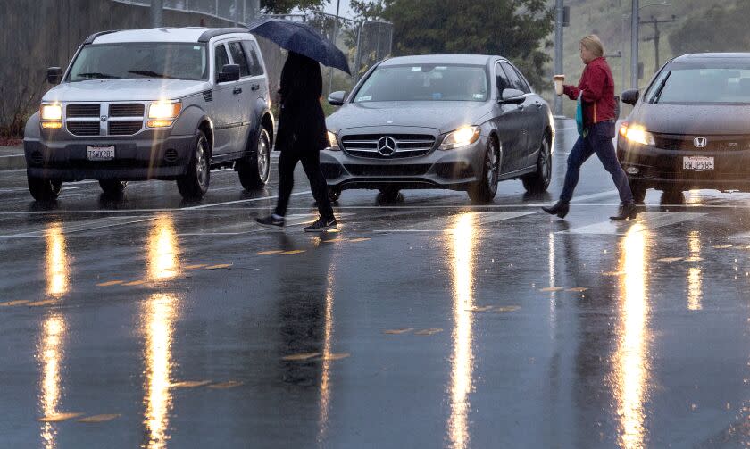 Los Angeles, CA - March 21: Pedestrians cross the road in the rain in El Sereno Tuesday, March 21, 2023. (Allen J. Schaben / Los Angeles Times)