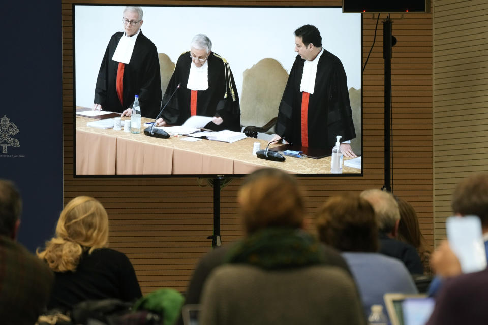 Reporters watch a screen showing Vatican tribunal president Giuseppe Pignatone reading the verdict of a trial against Cardinal Angelo Becciu and nine other defendants, in the Vatican press room, Saturday, Dec. 16, 2023. A once-powerful cardinal and nine other people are to learn their fates when a Vatican tribunal hands down verdicts in a complicated financial trial that has aired the tiny city state's dirty laundry. Judge Giuseppe Pignatone will read out the verdicts of the three-judge panel in the converted courtroom in the Vatican Museums on Saturday. (AP Photo/Andrew Medichini)