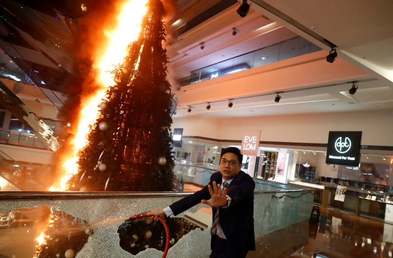 A man reacts as he tries to extinguish a burning Christmas tree at Festival Walk mall in Kowloon Tong, Hong Kong