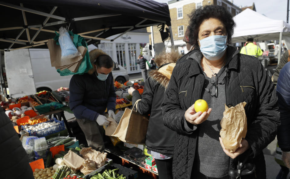 A woman wears a mask as she shops at a fruit and vegetable stall in Portobello Road market in London, Saturday, March 21, 2020. For most people, the new coronavirus causes only mild or moderate symptoms, such as fever and cough. For some, especially older adults and people with existing health problems, it can cause more severe illness, including pneumonia.(AP Photo/Kirsty Wigglesworth)