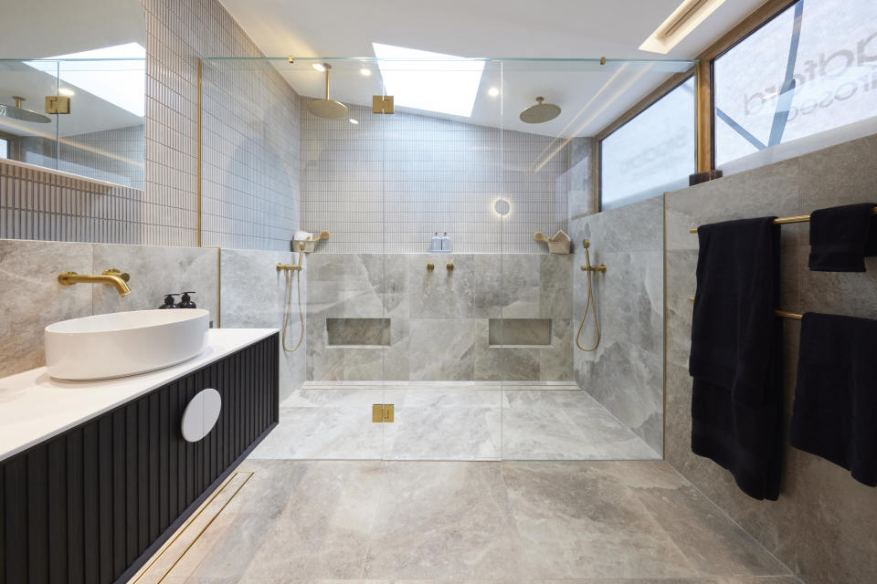 A wide shot of the bathroom with a vanity on the left, a double shower on the far wall and towel rack on the right. 