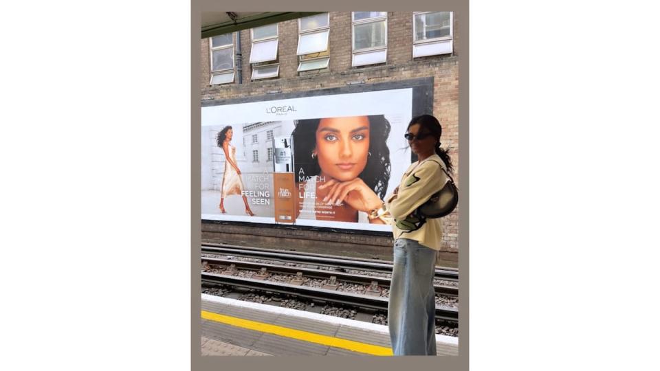 Simone Ashley poses in jeans and a sweatshirt infront of a Billboard