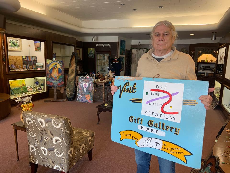 William Caouette holds a temporary sign for his art gallery at 33 Parker St. in Gardner. The shop, which he owns with his wife, Paula Abare, opened late in 2021.