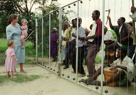 FILE PHOTO: Pippa van Rechteren and her twin daughters Catherine and Elizabeth watch farm invaders sing revolutionary songs outside the electric fence of their homestead on Chiripiro farm in Centenary district, Zimbabwe, March 29, 2000. REUTERS/Stringer/File Photo