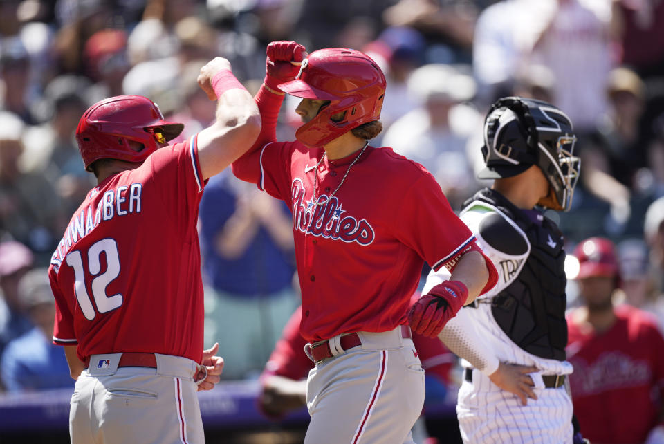 Philadelphia Phillies' Kyle Schwarber, left, congratulates Alec Bohm as he crosses home plate after hitting a two-run home run as Colorado Rockies catcher Dom Nunez waits for play to resume in the fourth inning of a baseball game Wednesday, April 20, 2022, in Denver. (AP Photo/David Zalubowski)