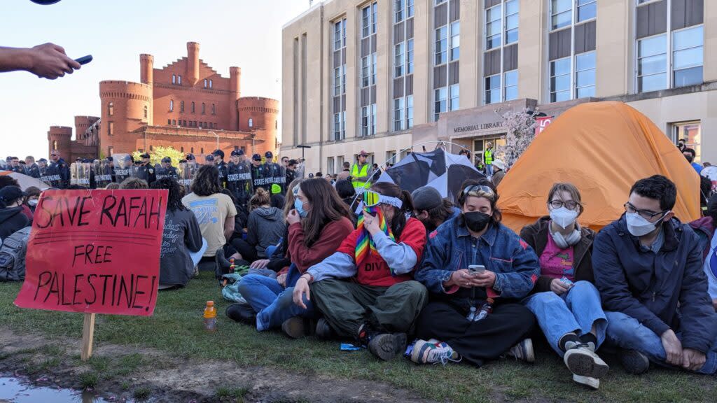 University of Wisconsin-Madison demonstrators sit on grass near tents as police work to dismantle their encampment.