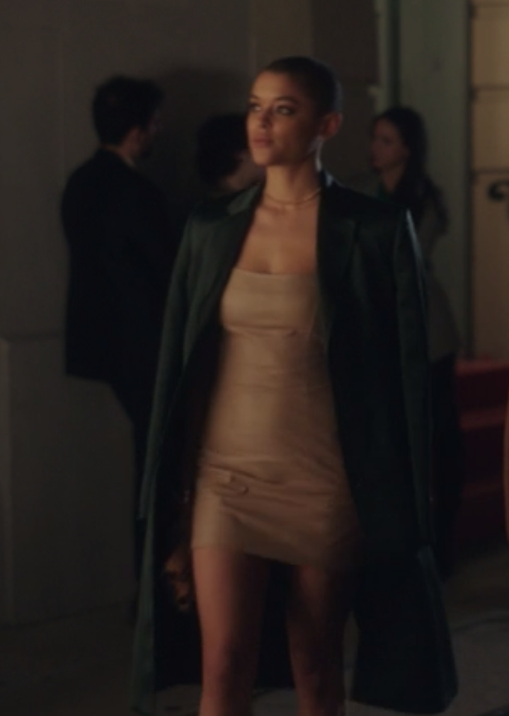 Julien wears a long dark trench coat over a tight fitted mini dress