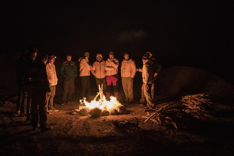 In this Sunday, Jan. 12, 2020 photo, Dakar pilots and medics gather around a bonfire after stage seven of the Dakar Rally in Wadi Al Dawasir, Saudi Arabia. Formerly known as the Paris-Dakar Rally, the race was created by Thierry Sabine after he got lost in the Libyan desert in 1977. Until 2008, the rallies raced across Africa, but threats in Mauritania led organizers to cancel that year's event and move it to South America. It has now shifted to Saudi Arabia. The race started on Jan. 5 with 560 drivers and co-drivers, some on motorbikes, others in cars or in trucks. Only 41 are taking part in the Original category. (AP Photo/Bernat Armangue)