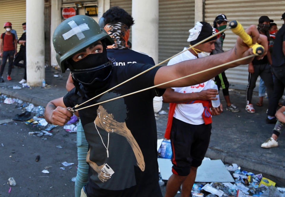 An anti-government protester throws a stone at security forces during clashes in the al-Rasheed street in Baghdad, Iraq, Friday, Nov. 8, 2019. The demonstrators complain of widespread corruption, lack of job opportunities and poor basic services, including regular power cuts despite Iraq's vast oil reserves. They have snubbed limited economic reforms proposed by the government, calling for it to resign. (AP Photo/Khalid Mohammed)