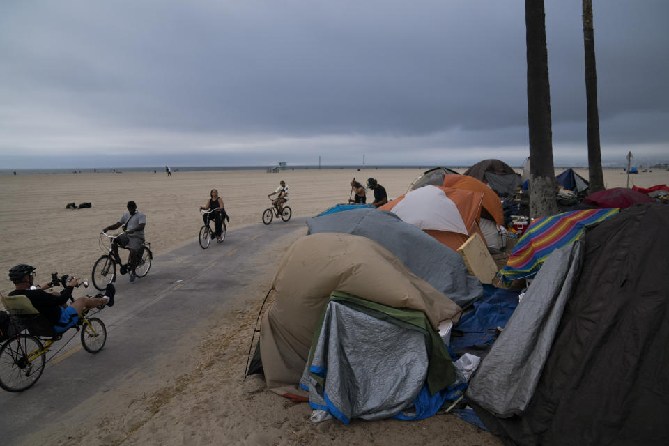 FILE - People ride their bikes past a homeless encampment set up along the boardwalk in the Venice neighborhood of Los Angeles, June 29, 2021. An alternative mental health court program designed to fast-track people with untreated schizophrenia into housing and medical care starts in San Francisco and six other California counties. (AP Photo/Jae C. Hong, File)