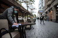 An employee wearing a mouth and nose protector wipes tables in a restaurant on the shopping street Koenigsallee in Duesseldorf, Germany, Friday, Oct. 9, 2020. The corona pandemic is increasingly becoming a problem in the large cities and conurbations of North Rhine-Westphalia. (Fabian Strauch/dpa via AP)