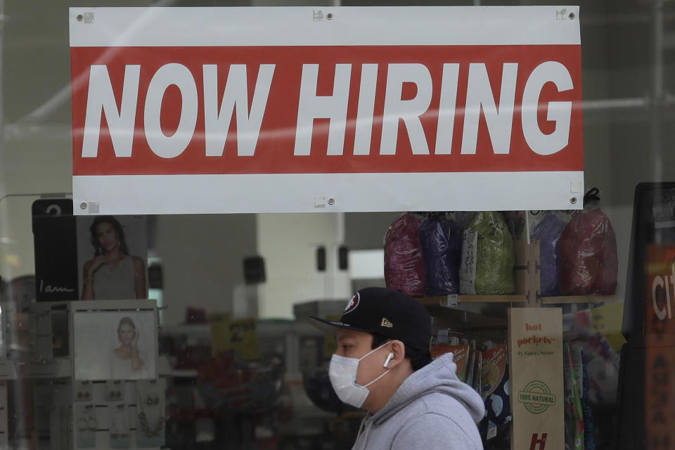 FILE - This May 7, 2020, file photo shows a man wearing a mask while walking under a Now Hiring sign at a CVS Pharmacy during the coronavirus outbreak in San Francisco.  On Thursday, Nov. 12, the number of people seeking unemployment benefits fell last week to 709,000, the fourth straight drop and a sign that the job market is slowly healing. The figures coincide with a sharp resurgence in confirmed viral infections to an all-time high above 120,000 a day.  (AP Photo/Jeff Chiu, File)