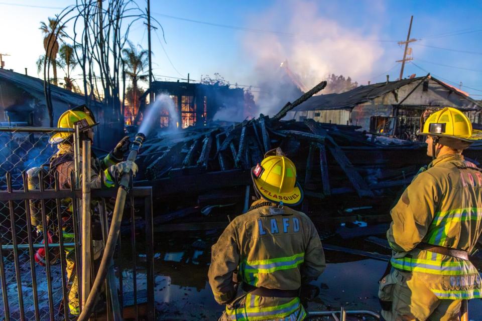 Firefighters spray water on a smoldering pile of timber from a collapsed construction framing