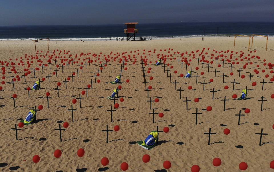 Crosses and red balloons are placed in the sand on Copacabana beach in a demonstration organized by Rio de Paz to honor the victims of COVID-19, as the country heads to a milestone of 100,000 new coronavirus related deaths, in Rio de Janeiro, Brazil, Saturday, Aug. 8, 2020. (AP Photo/Mario Lobao)