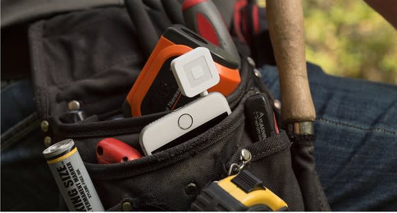 Square credit card reader attached to a mobile phone.