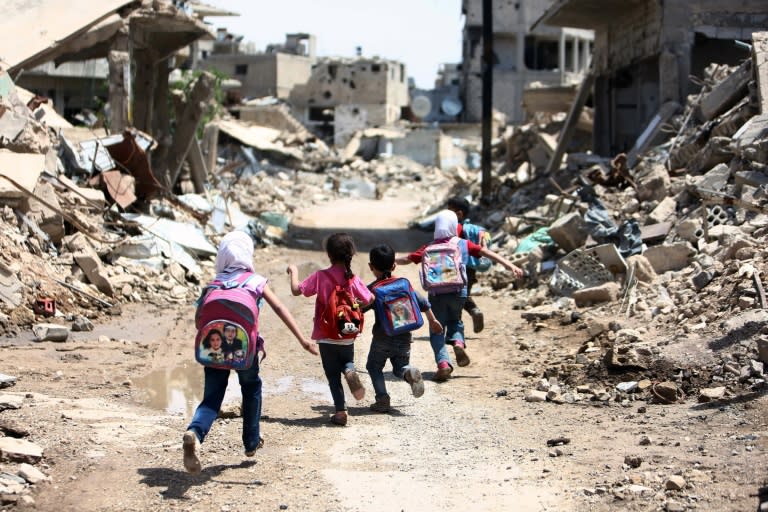 Syrian schoolchildren run past damaged buildings in the rebel-held are of Jobar, on the eastern outskirts of the capital Damascus, on April 30, 2016