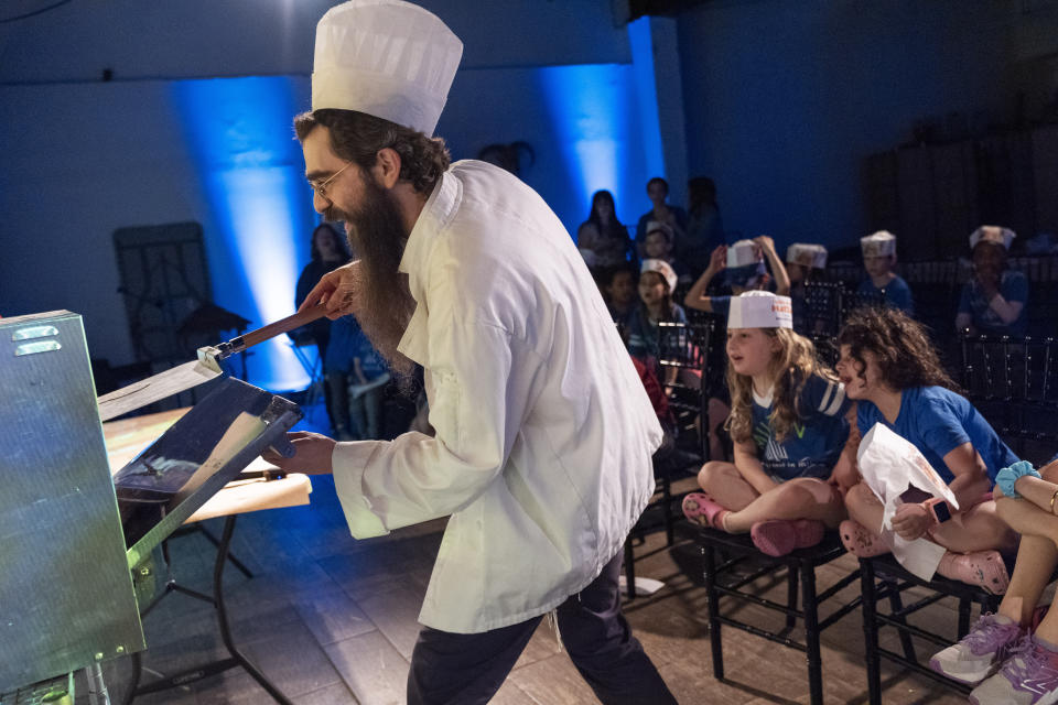 Rabbi Levi Raskin, director of the JCrafts Center for Jewish Life and Tradition, playfully adds flat discs of dough to the oven to cook into matzah, as prepared by first graders from Milton Gottesman Jewish Day School of the Nation's Capital, during a "Model Matzah Factory" field trip at the center in Rockville, Md., Thursday, April 18, 2024. To be kosher for the Passover holiday, which begins Monday evening, the dough has to be prepared and cooked all within 18 minutes and not allowed to rise. (AP Photo/Jacquelyn Martin)